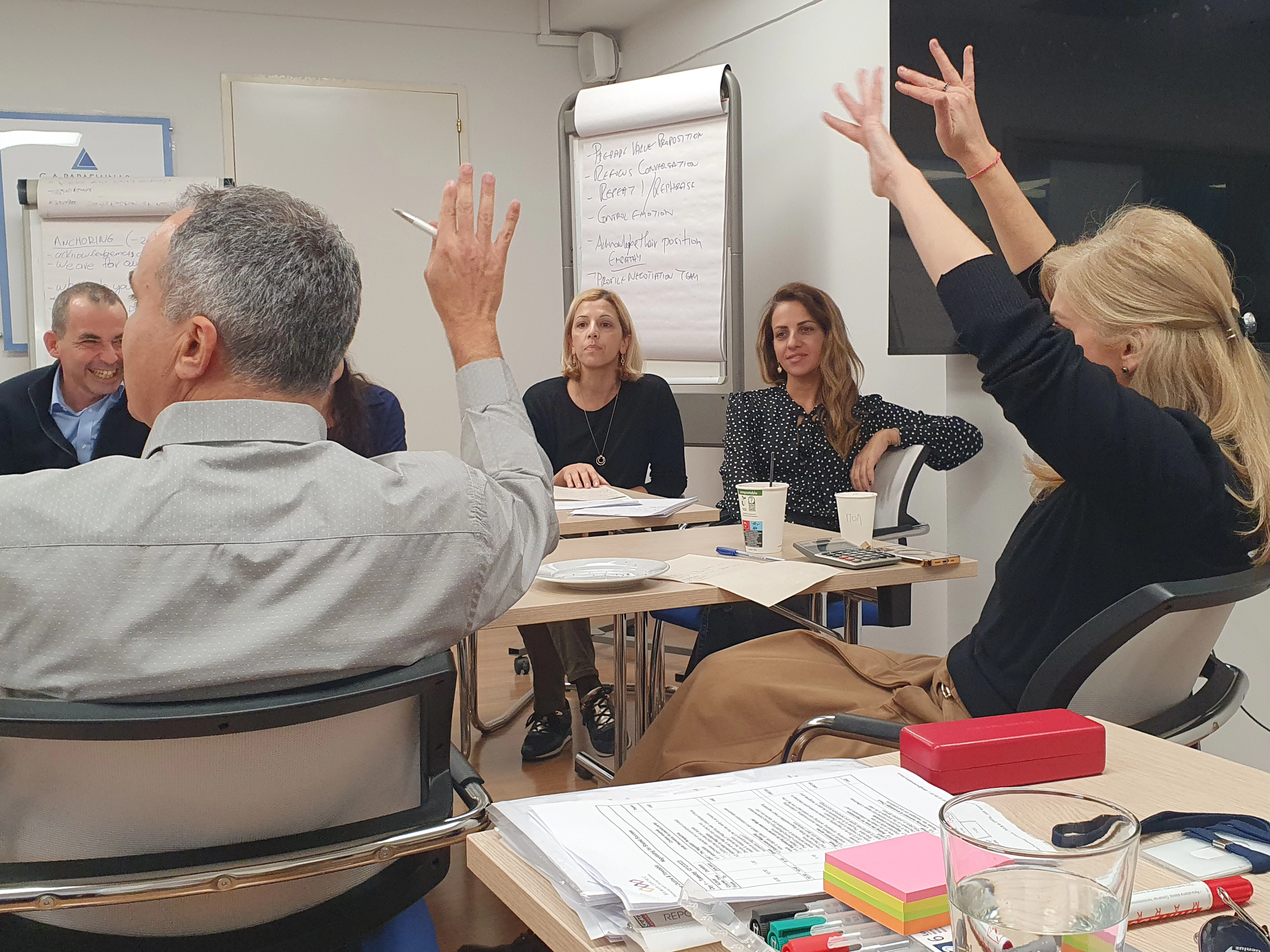 Negotiation skills training session with enthusiastic participants raising hands and enjoying the interactive seminar.