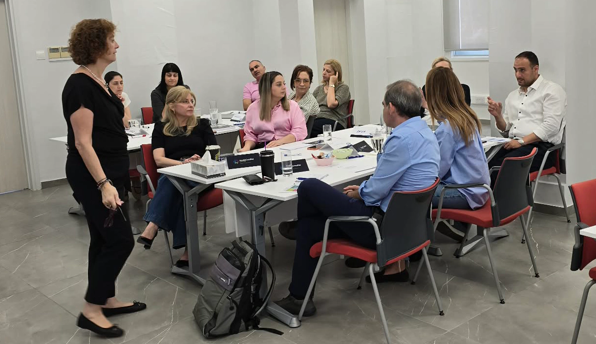 Facilitator presenting to a seated group of pharma professionals in a modern training room.