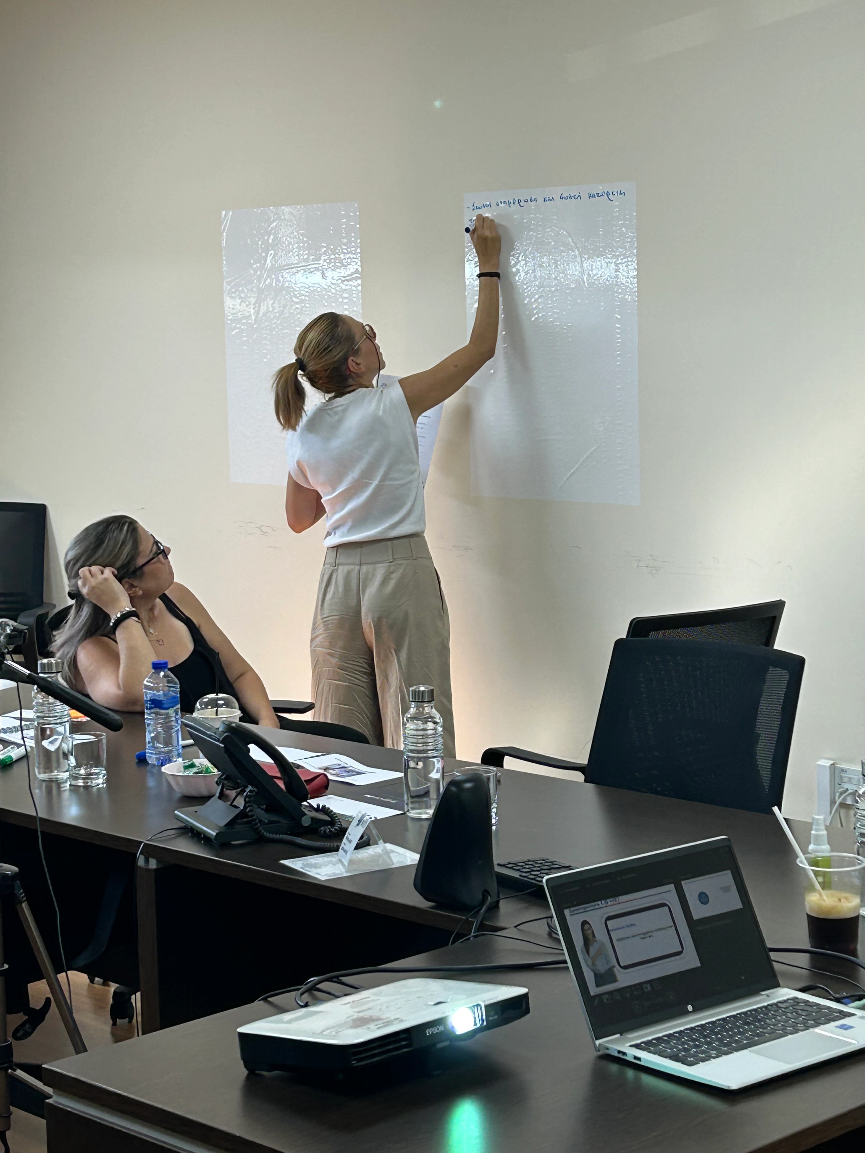 Professional woman writing on the wall while a colleague watches attentively.