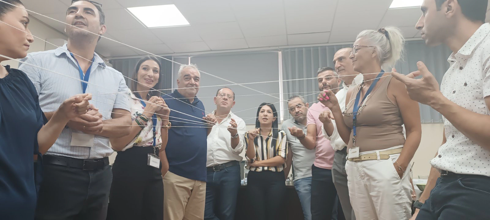 Workshop participants standing in a group, holding a single string to illustrate teamwork and interconnected roles during a practical exercise.