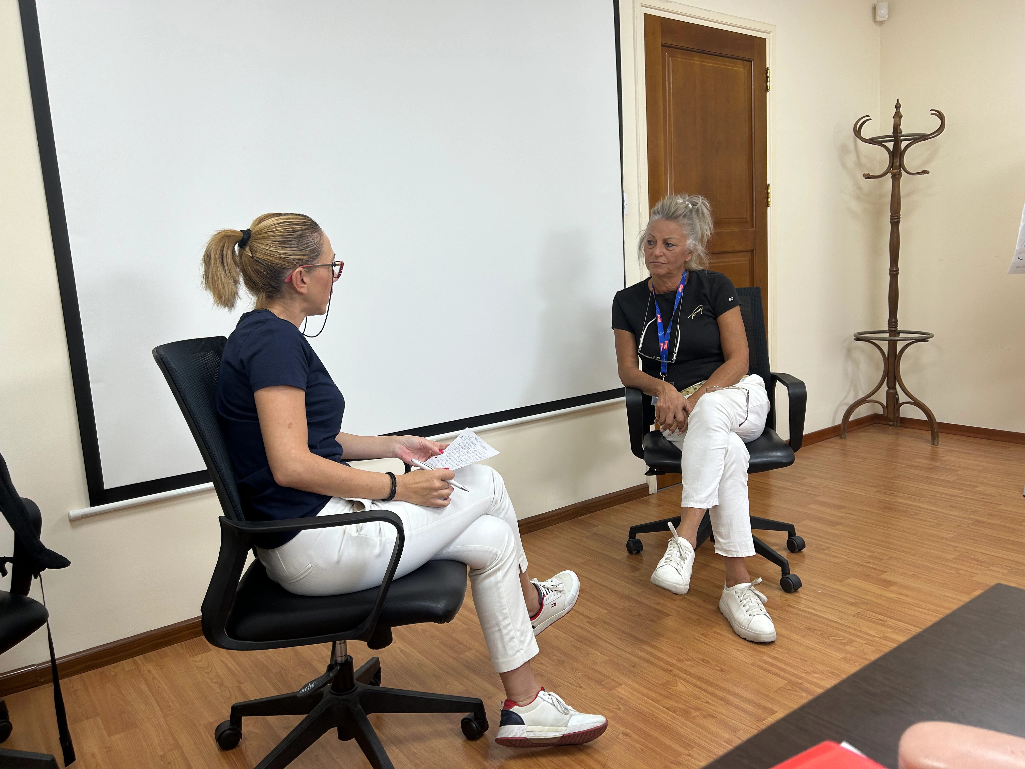Two professional women seated on office chairs, engaging in an interactive dialogue during the workshop.